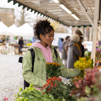 Eine junge Frau betrachtet Blumen an einem Marktstand.